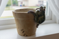 Green frog figurine on a small stone pot on a wooden shelf.
