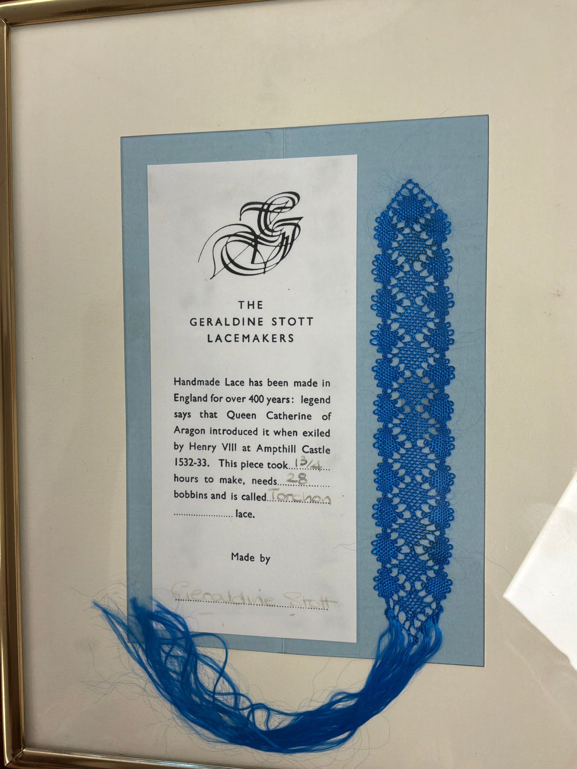 Framed piece of lace with text about the Geraldine Stott Lacemakers on a light blue background.
