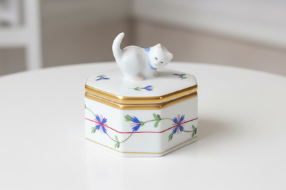 Decorative hexagonal box with floral patterns and a small white cat figurine on top, set against a neutral background.
